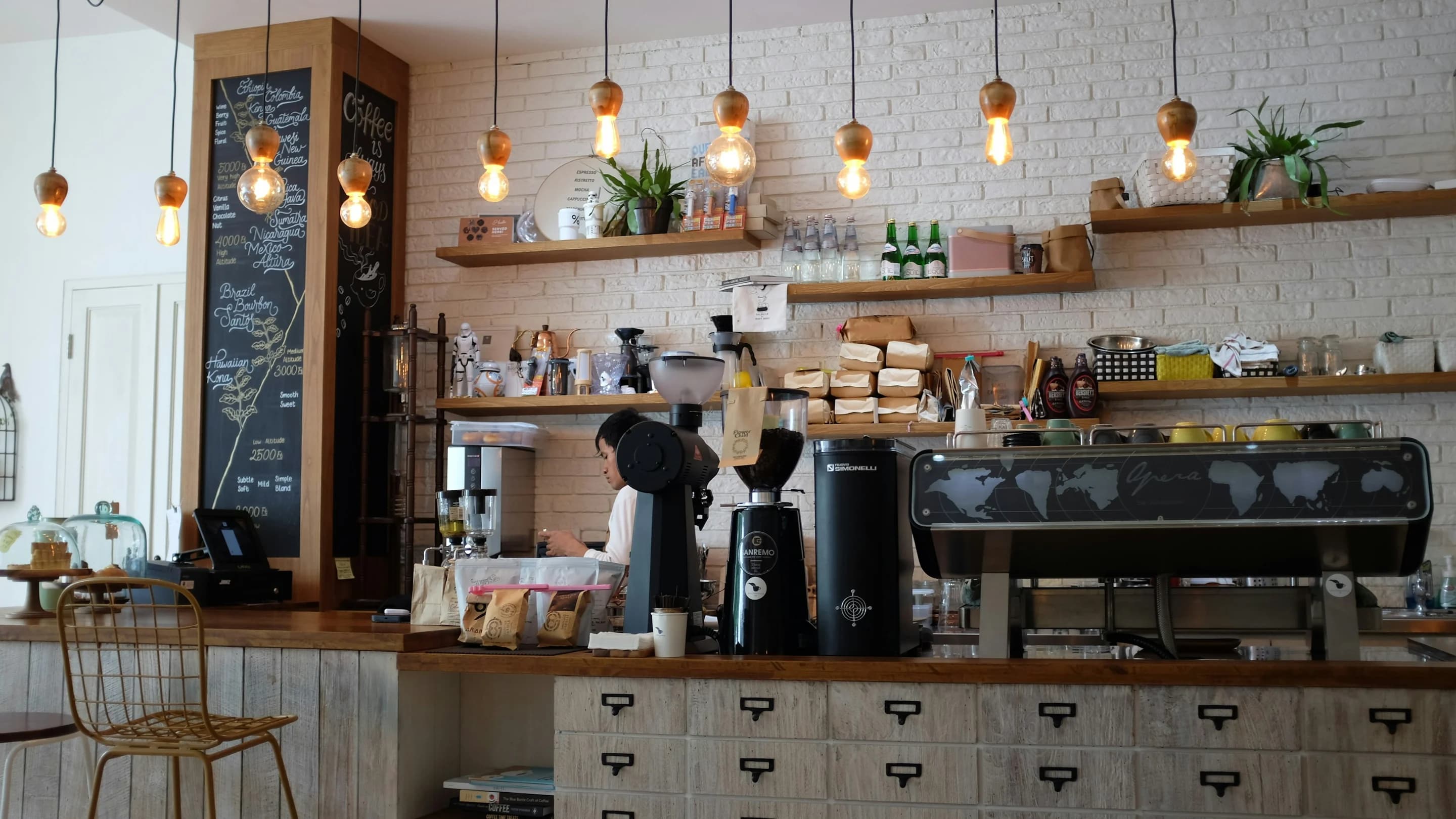Barra de una cafetería con cafetera espresso y repisas de madera
